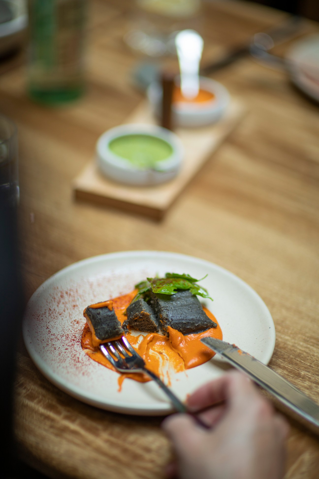Plated dish with charred nori, orange sauce, and microgreens, with sauce bowls blurred in background.