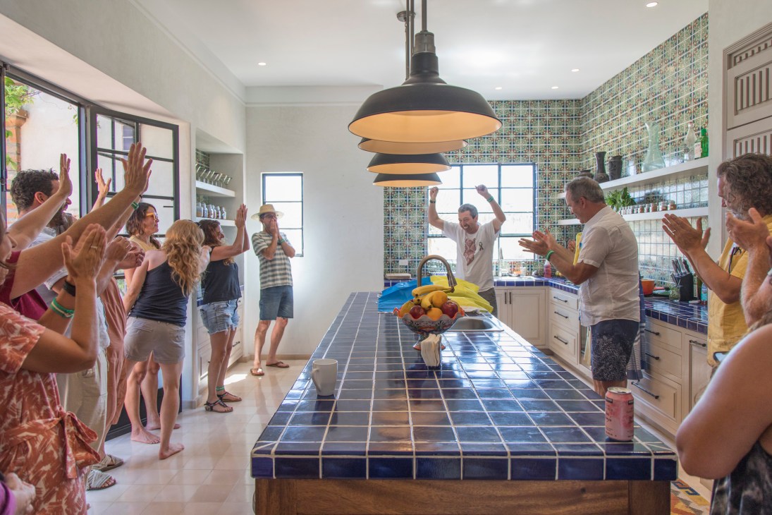 Group of people clapping and celebrating around a kitchen island with a man raising his arms in the center