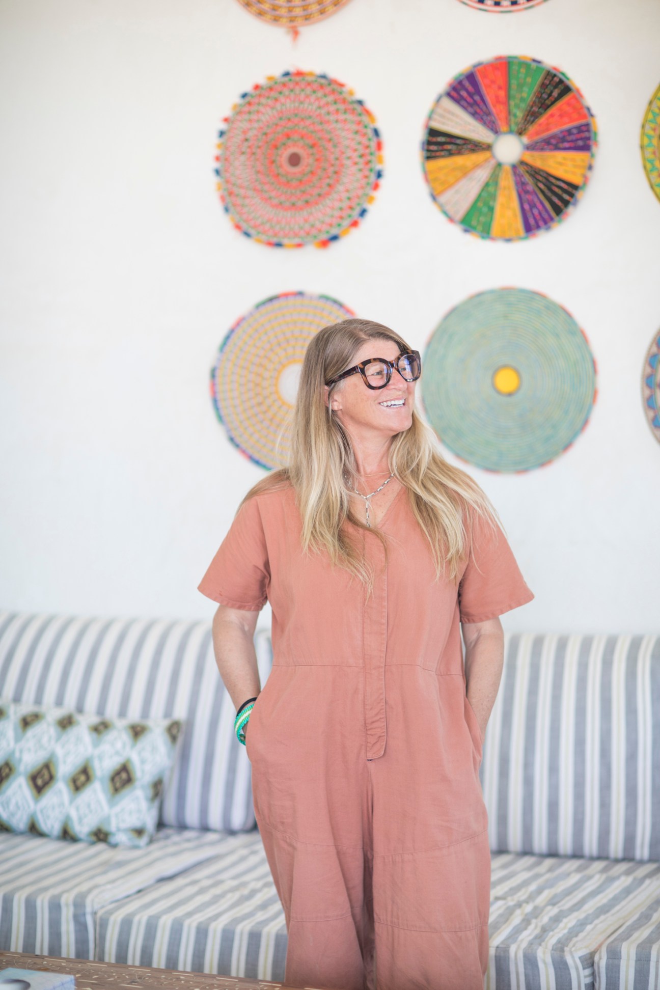 Portrait of Christine Sperber, co-founder of Modern Elder Academy in coral jumpsuit standing in front of colorful circular wall art
