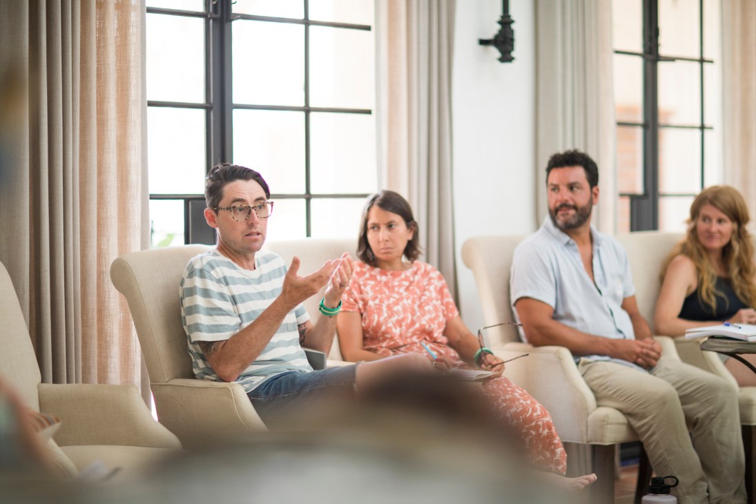 Four adults sitting on beige sofas in bright living room during what appears to be a discussion or meeting