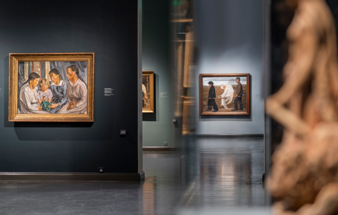 Gallery interior with framed paintings on dark walls and sculpture in foreground
