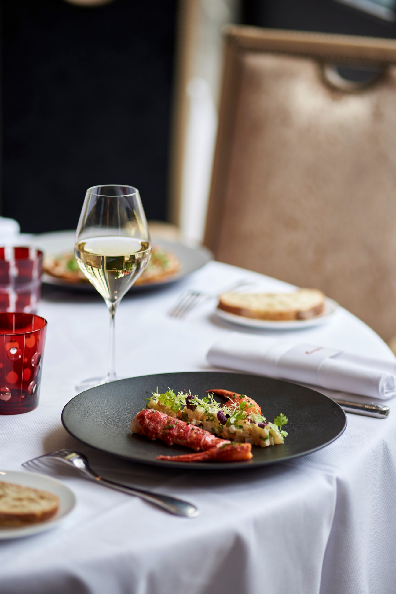 Fine dining table setting with white wine glass, plated seafood dish with garnish, and bread plates at Hotel Barrière Le Majestic Cannes.