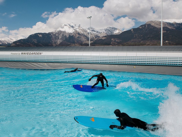 Surfer riding a wave in an inland surf pool with mountains behind.