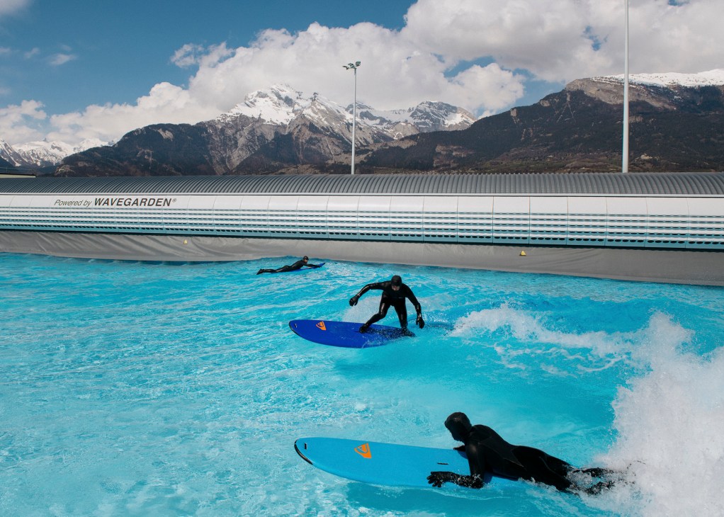 Surfer riding an artificial wave at Alaïa Bay with Swiss Alpine landscape in background
