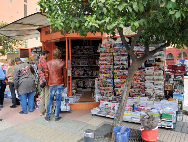 People browsing a busy street newsstand stacked with magazines.