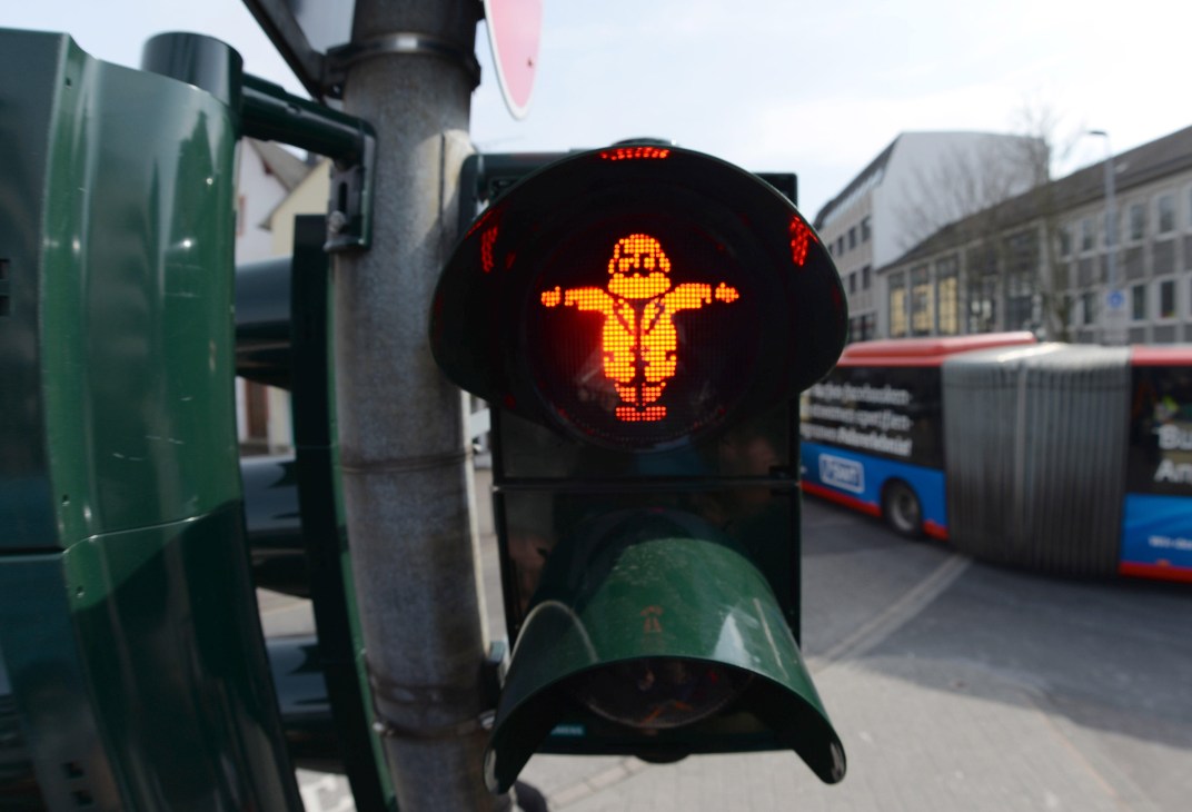 Red pedestrian traffic light showing a figure with arms outstretched in Karl Marx commemoration in Trier, Germany.