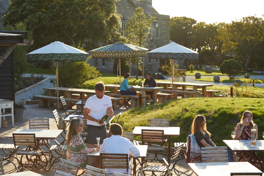 Outdoor dining area with wooden tables and umbrellas at The Pig at Harlyn Bay hotel