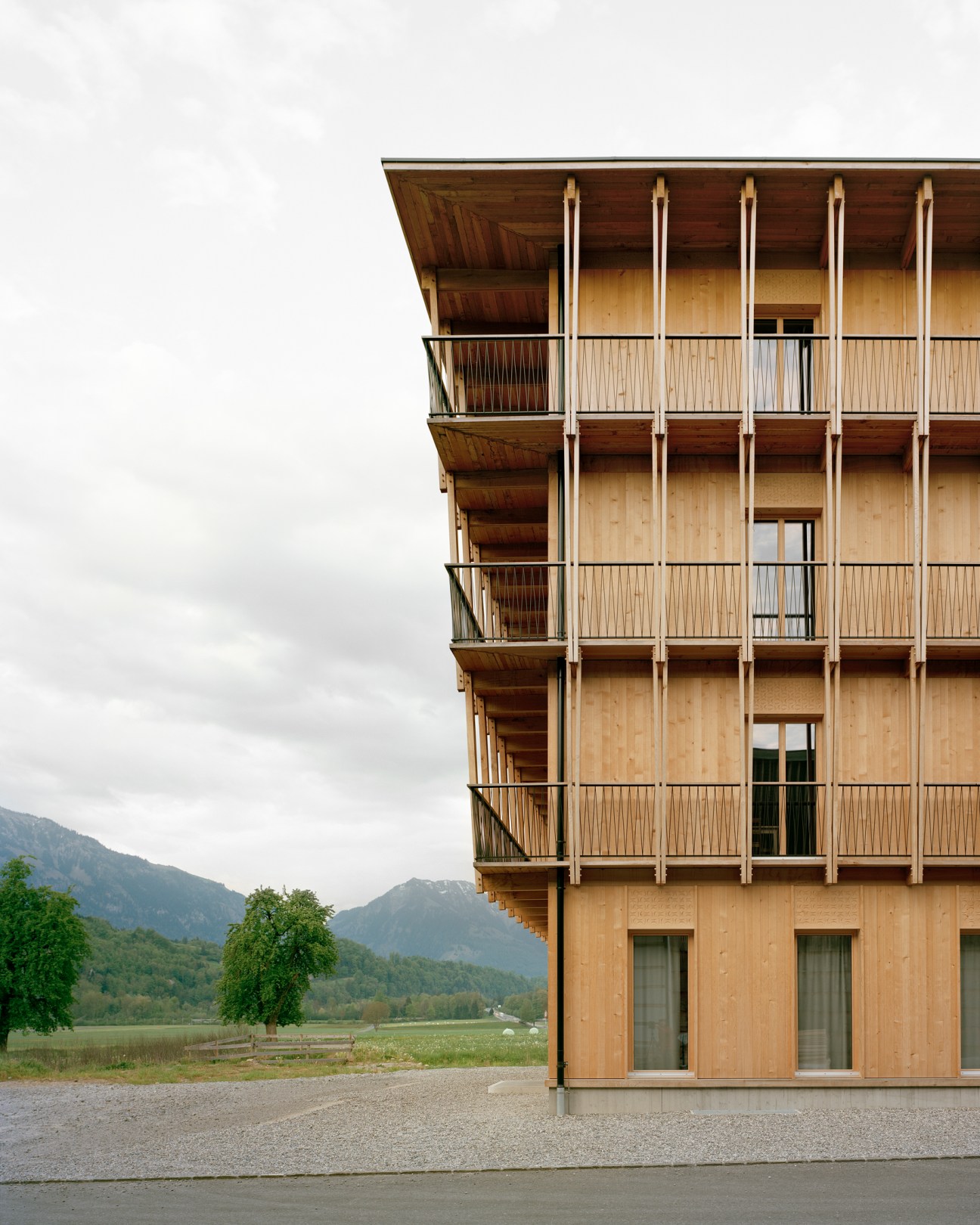 Küng Holzbau timber building with wooden balconies and vertical slats set against mountain landscape