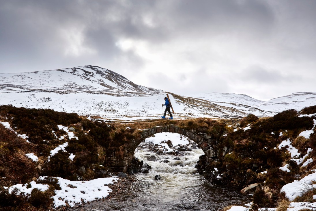 Jamie Kunka skiing across snowy terrain on a stone bridge in Scotland's Cairngorms mountains