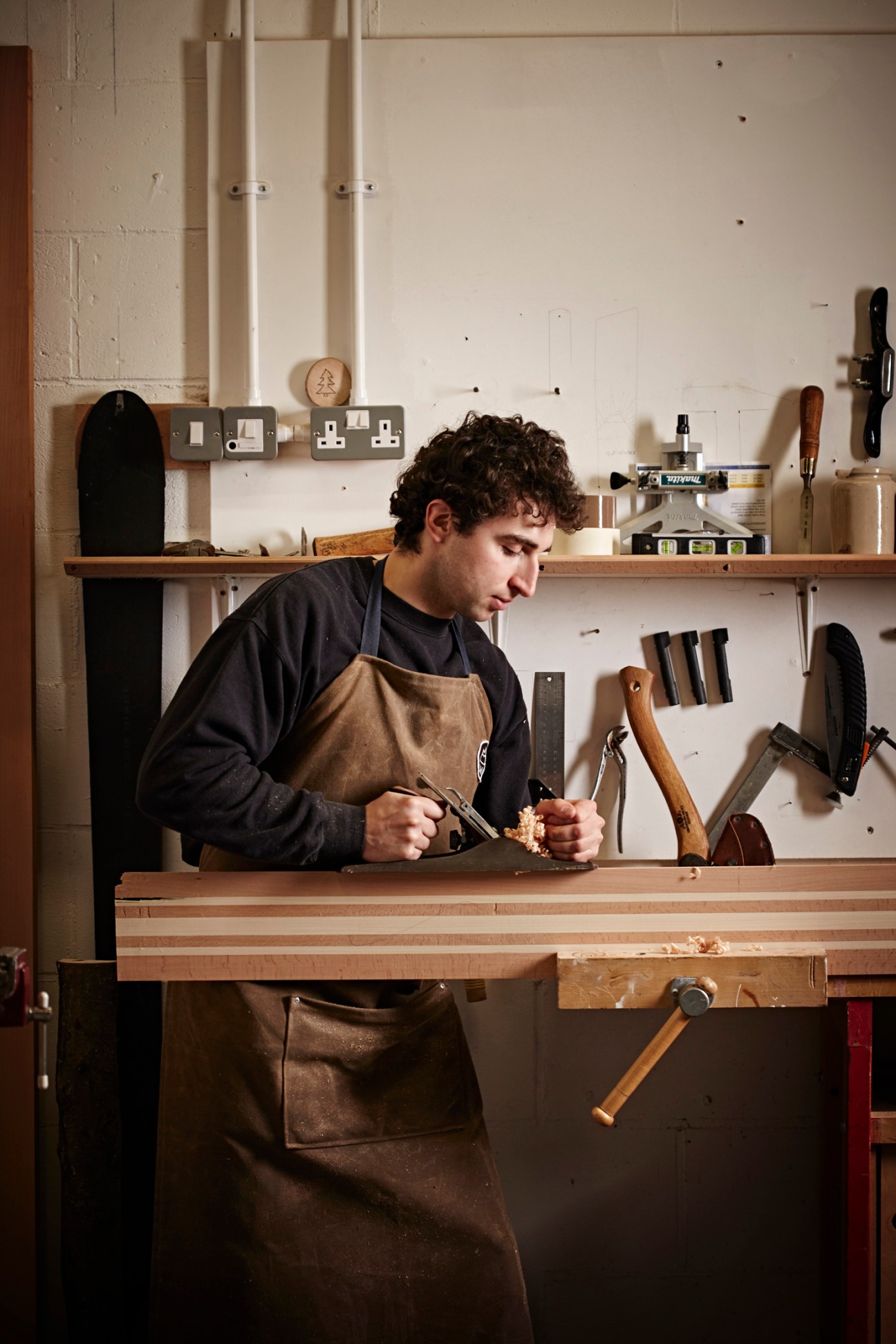 Jamie Kunka using a hand plane on wood at his workbench in his Scottish ski-making workshop
