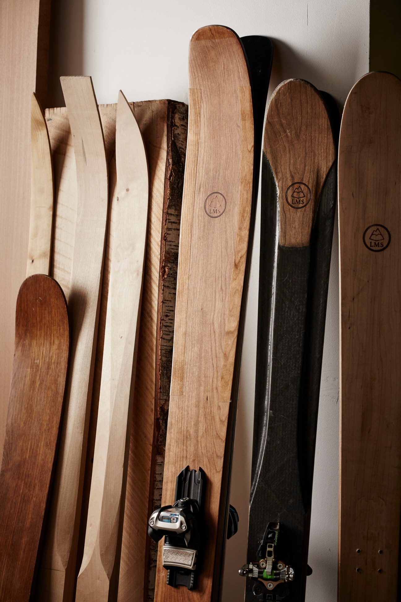 Collection of handcrafted wooden skis leaning against a white wall showing natural wood grain and craftsmanship