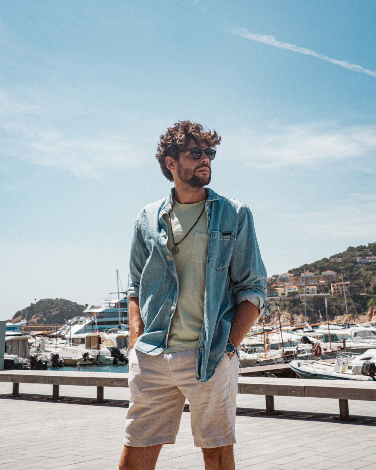 Álvaro Soler stands at a marina wearing a denim shirt and sunglasses, with boats in the background.