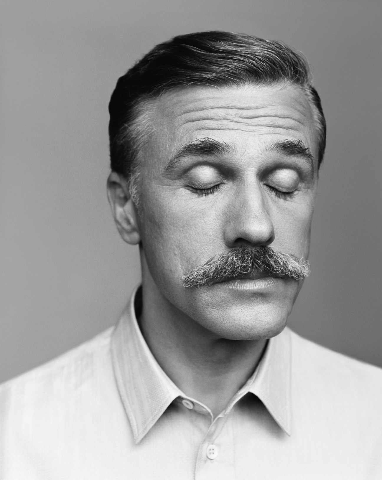 Black and white portrait of actor Christoph Waltz with eyes closed in dramatic fashion photography