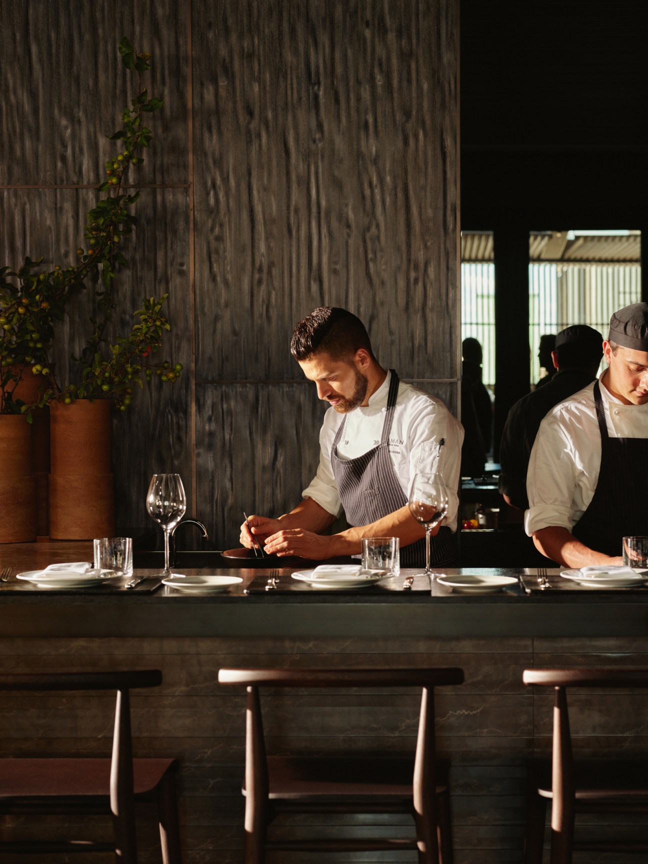 Chef at Aman New York's restaurant Arva plating dishes at counter with wine glasses and place settings