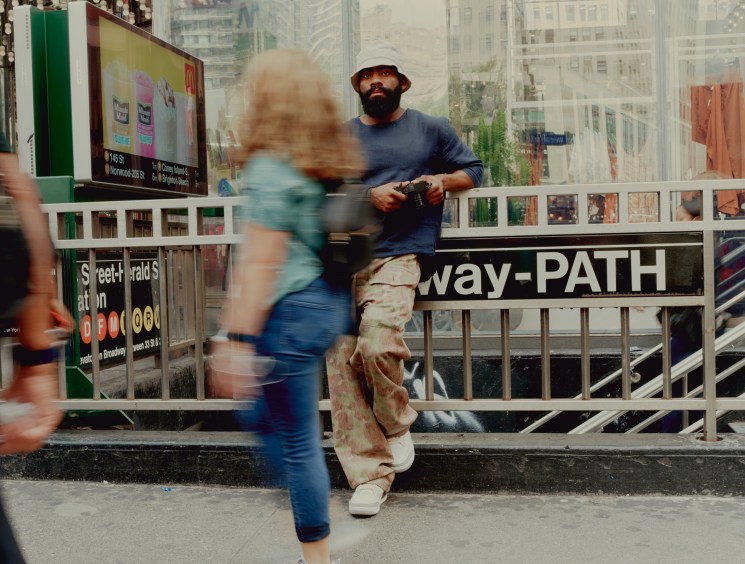 Street photographer Andre D Wagner leaning against subway station railing wearing bucket hat and casual clothes
