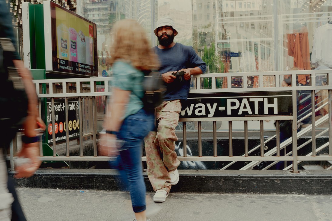 Street photographer Andre D Wagner leaning against subway station railing wearing bucket hat and casual clothes