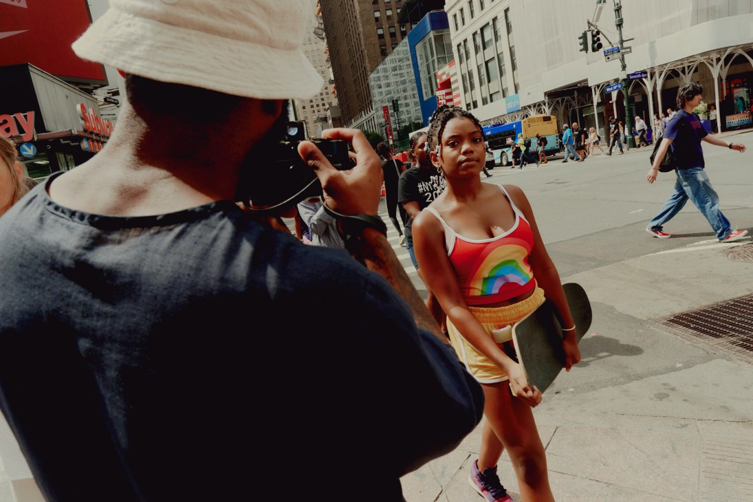 Street photographer taking a photograph of a young woman in colorful clothing on a busy New York sidewalk