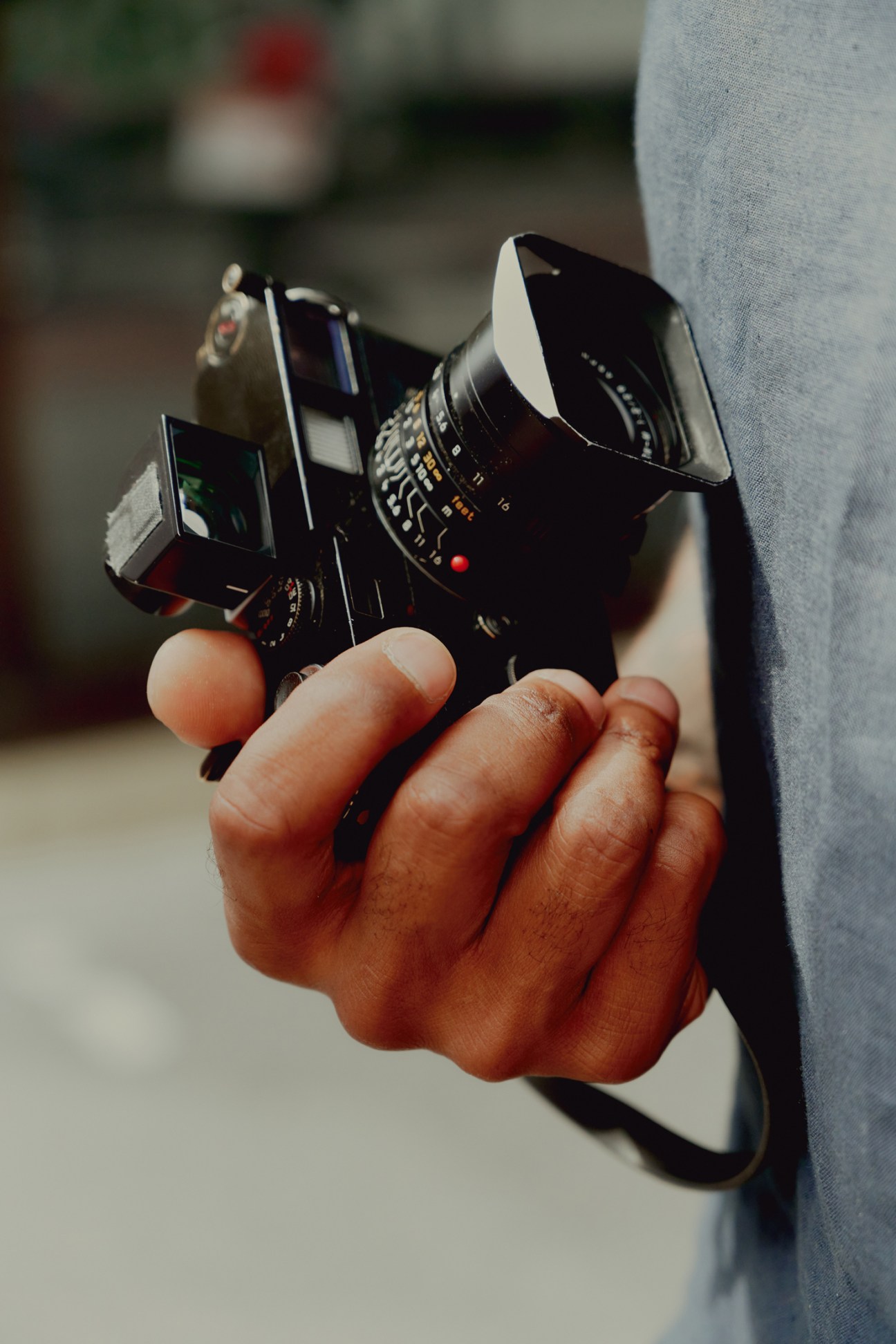 Close-up of hands holding a vintage Leica camera with lens hood and viewfinder