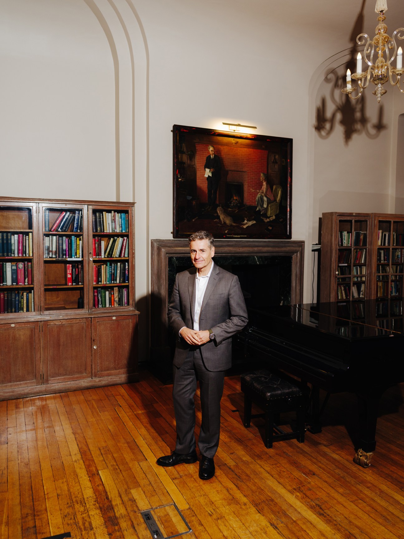 Andrés Velasco standing in an elegant library with wooden bookshelves, fireplace, and ornate chandelier