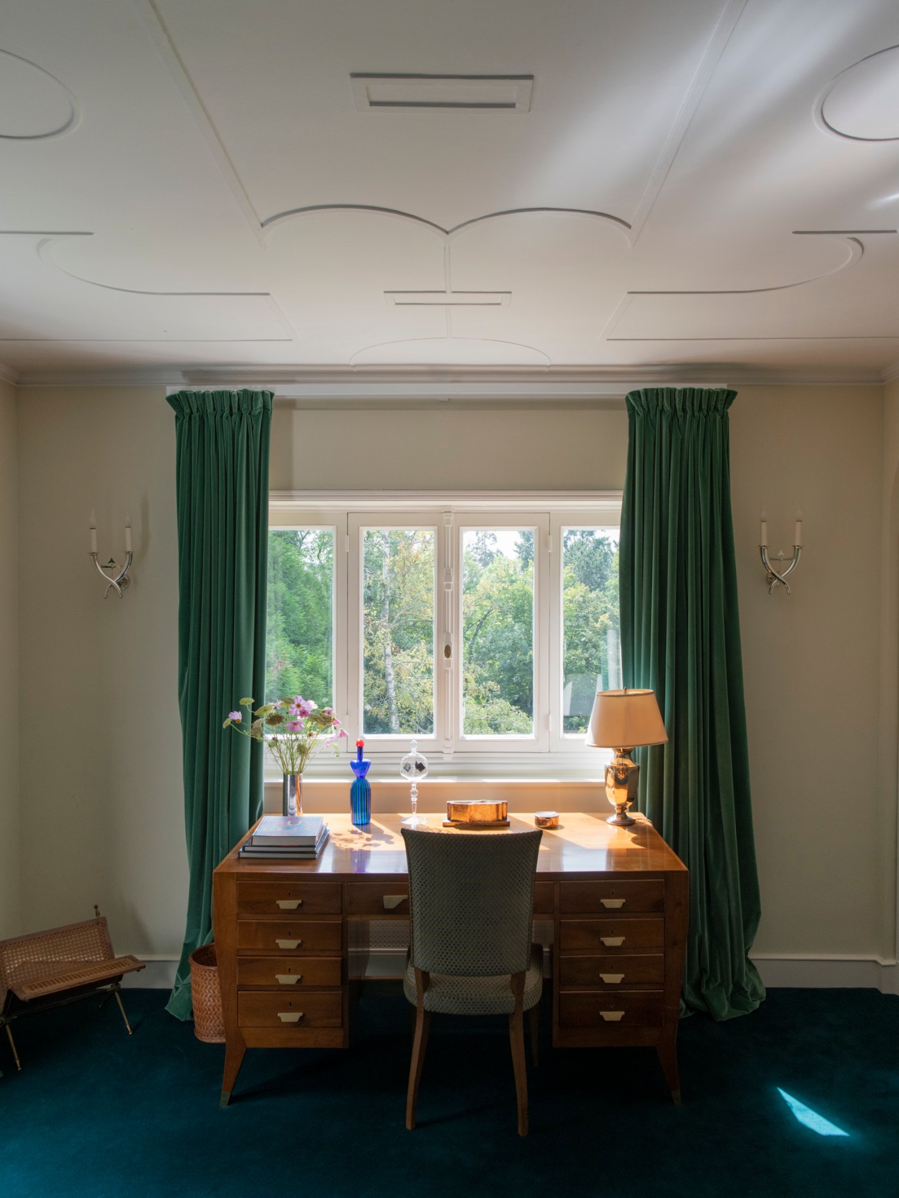 Home office with wooden desk, green curtains, ornate ceiling molding, and window overlooking garden