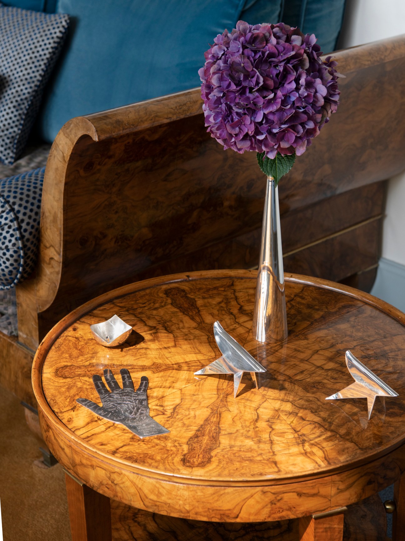 Decorative objects including silver sculptures and a purple hydrangea flower displayed on a wooden round table
