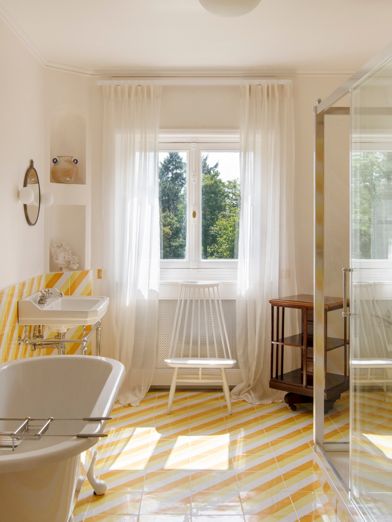 Bathroom with yellow and white geometric painted tiles on floor and walls, white fixtures, and window with curtains