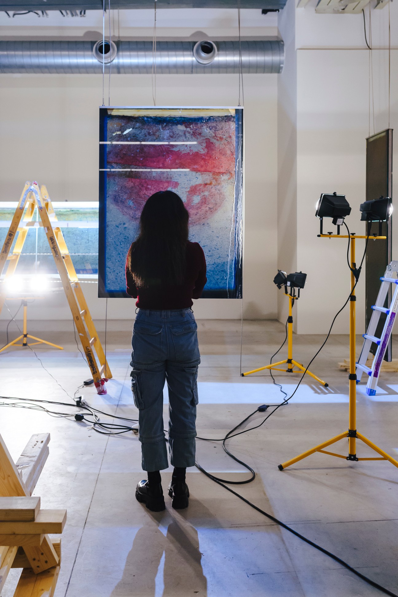 Person viewing a suspended glass display case containing colorful abstract artwork with blue, purple, and red tones in a gallery space