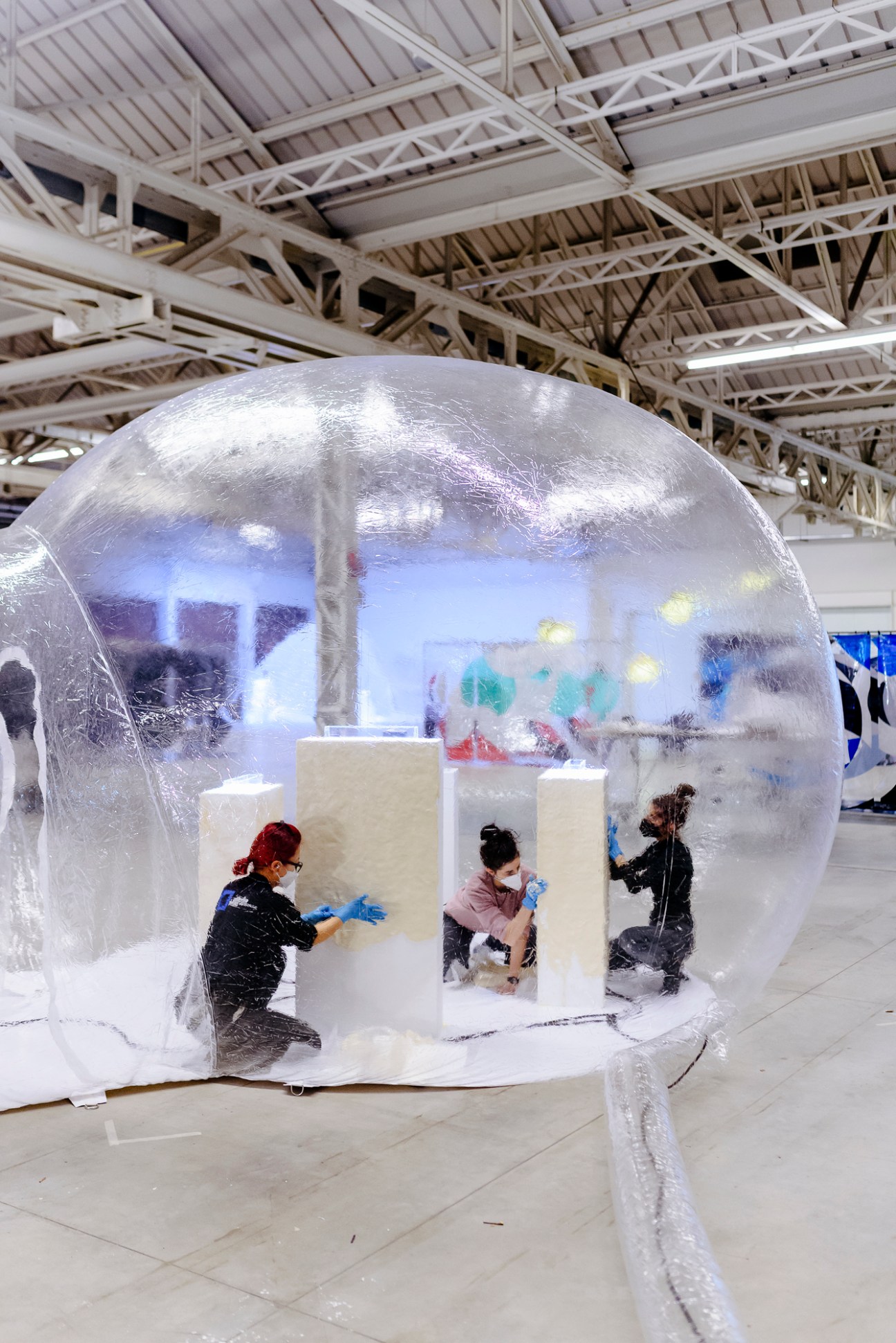 People working inside a large translucent spherical art installation with white cylindrical structures.
