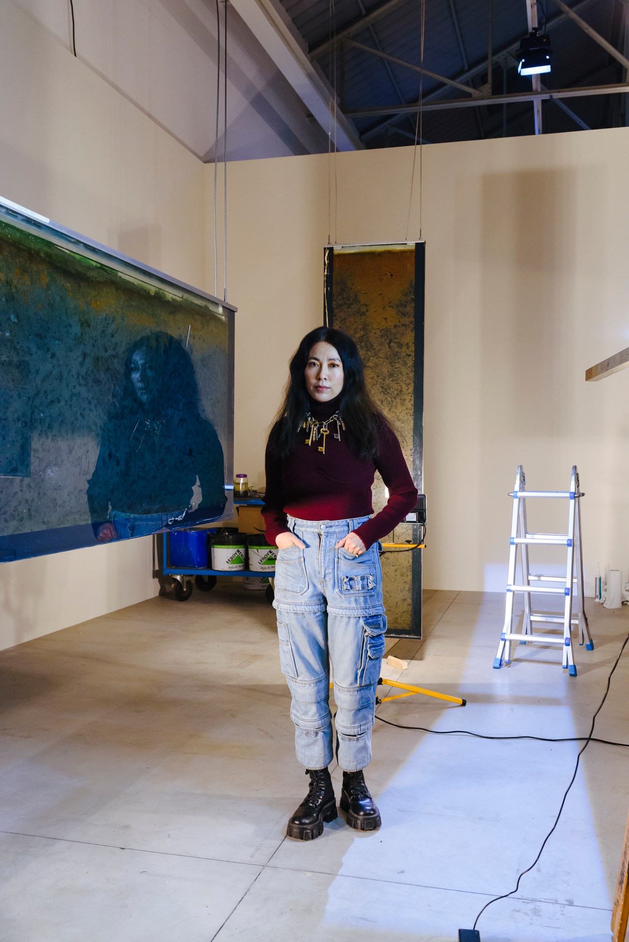 Artist Anicka Yi stands in her exhibition at Pirelli Hangar Bicocca, surrounded by suspended painted panels and installation materials.