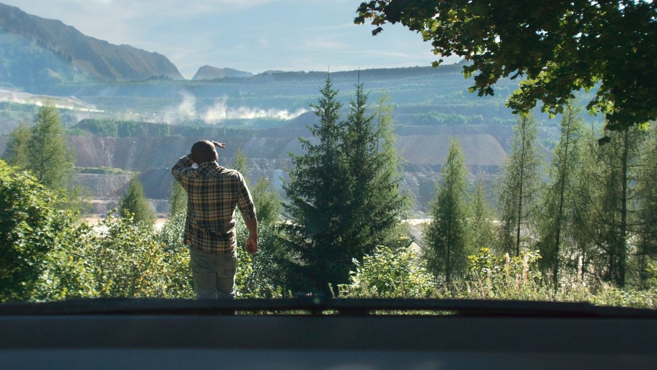 A man in plaid shirt looking out over mountainous Austrian landscape with trees in foreground