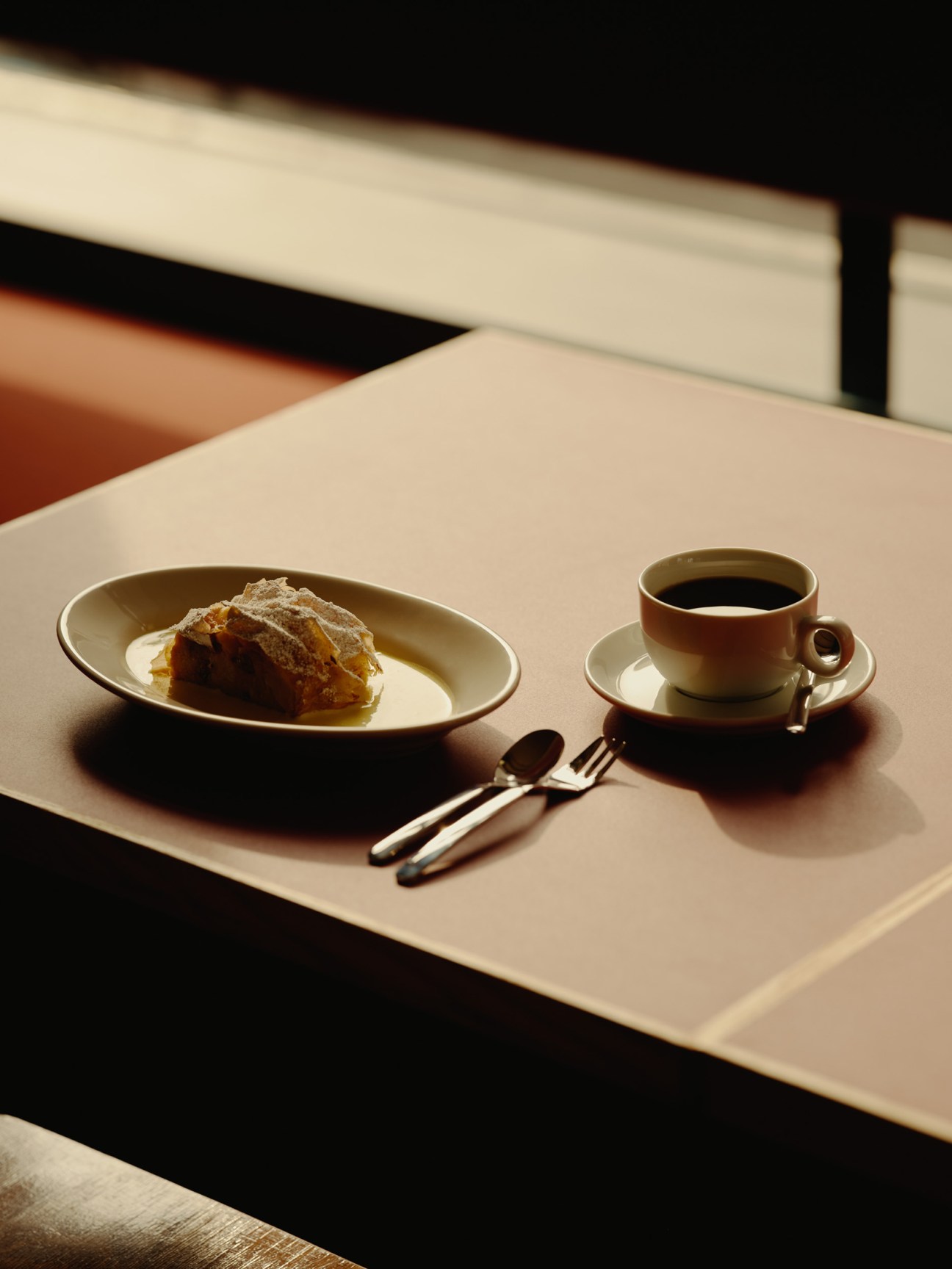 Apple strudel dessert with powdered sugar dusting served on cream-colored plate with coffee cup and utensils