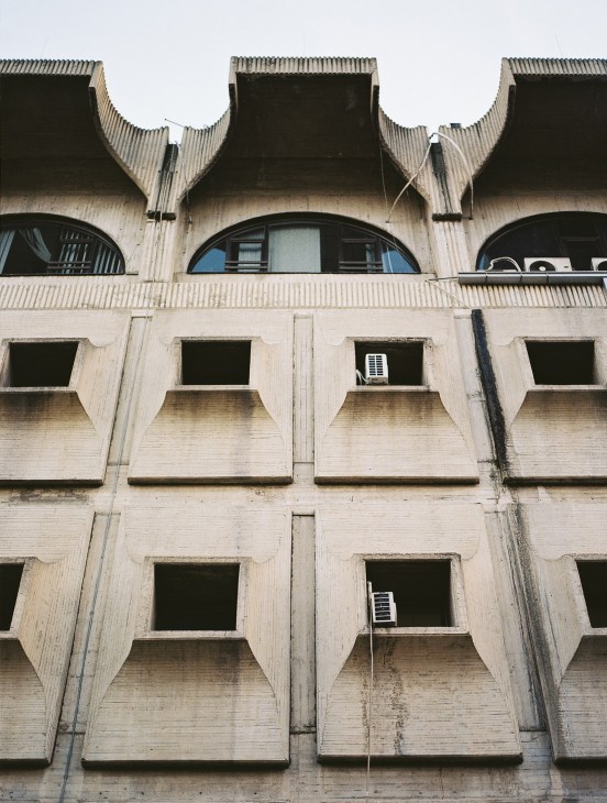 Brutalist concrete building facade with distinctive angular balconies and arched windows on upper floor