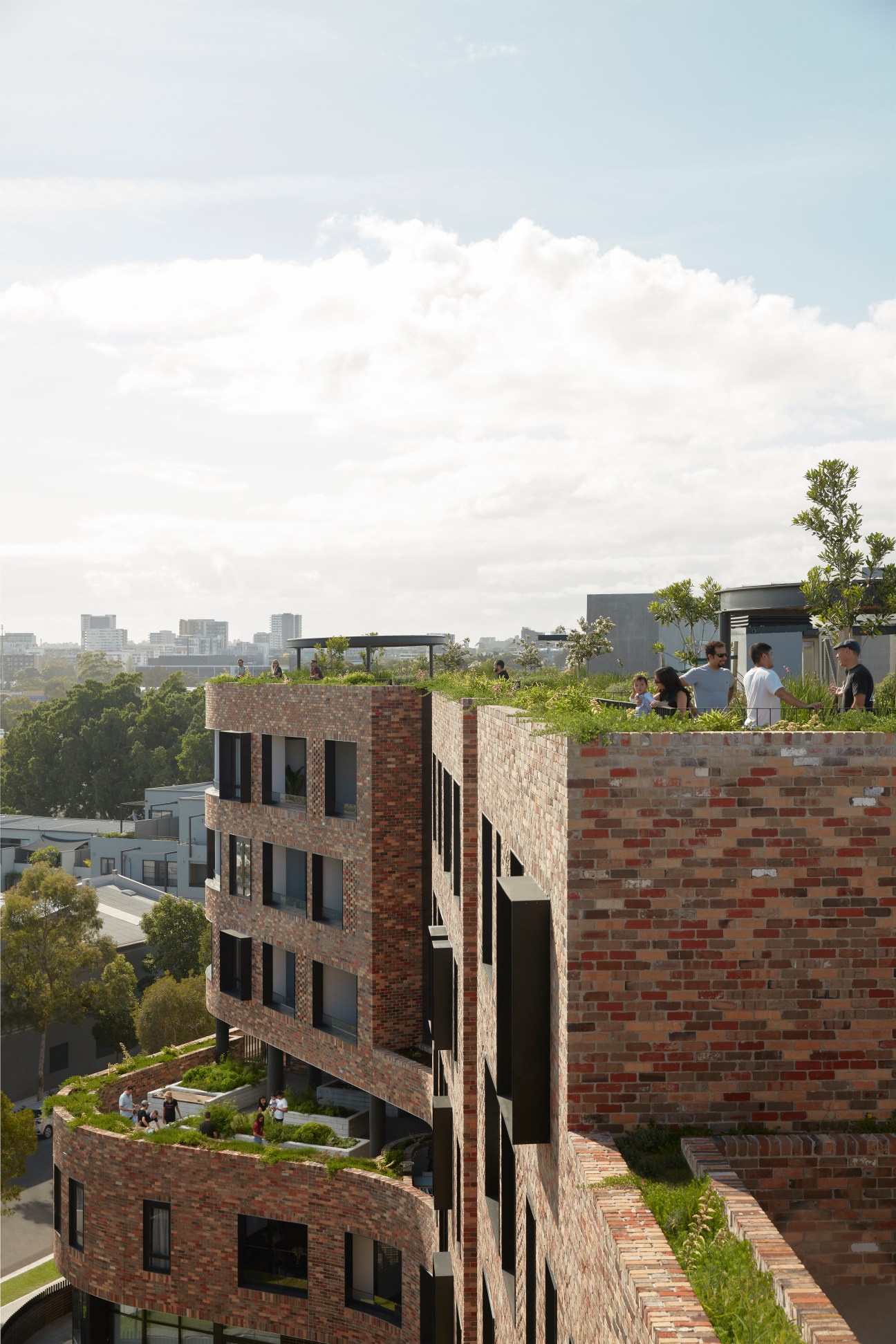 Aerial view of multi-story brick apartment buildings with rooftop gardens and people gathered on terraces