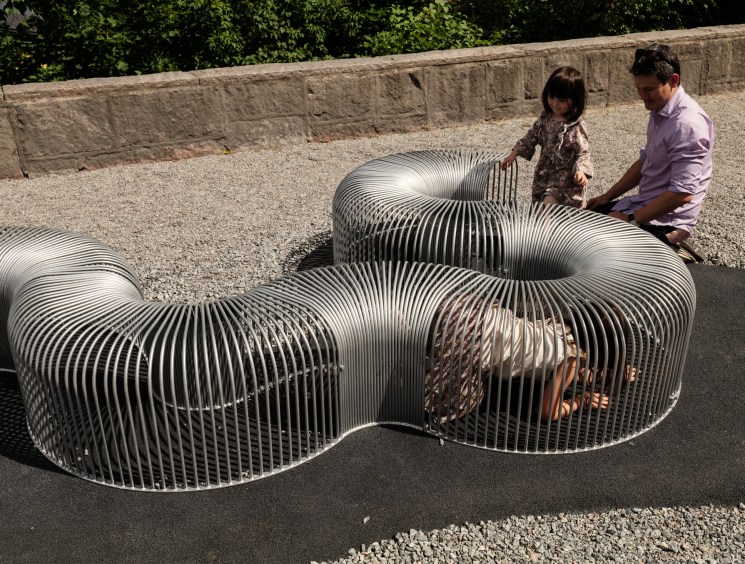 Children and adults interact with ribbed steel furniture structures in the garden at Stockholm's Arkdes museum