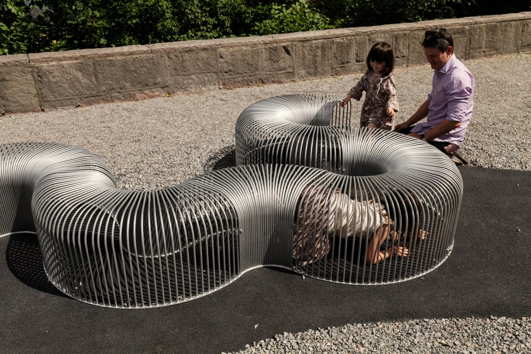 Children and adults interact with ribbed steel furniture structures in the garden at Stockholm's Arkdes museum