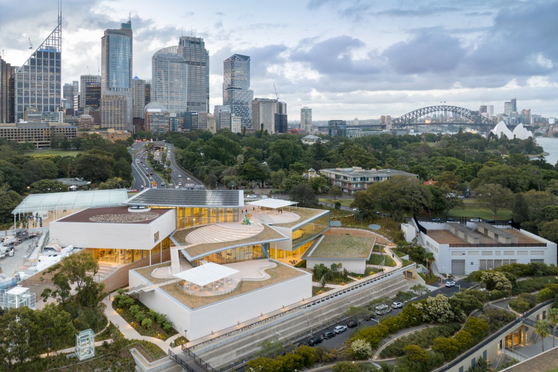 Aerial view of Sydney Modern gallery showing cascading glass and limestone pavilions amid parkland with Sydney's skyline