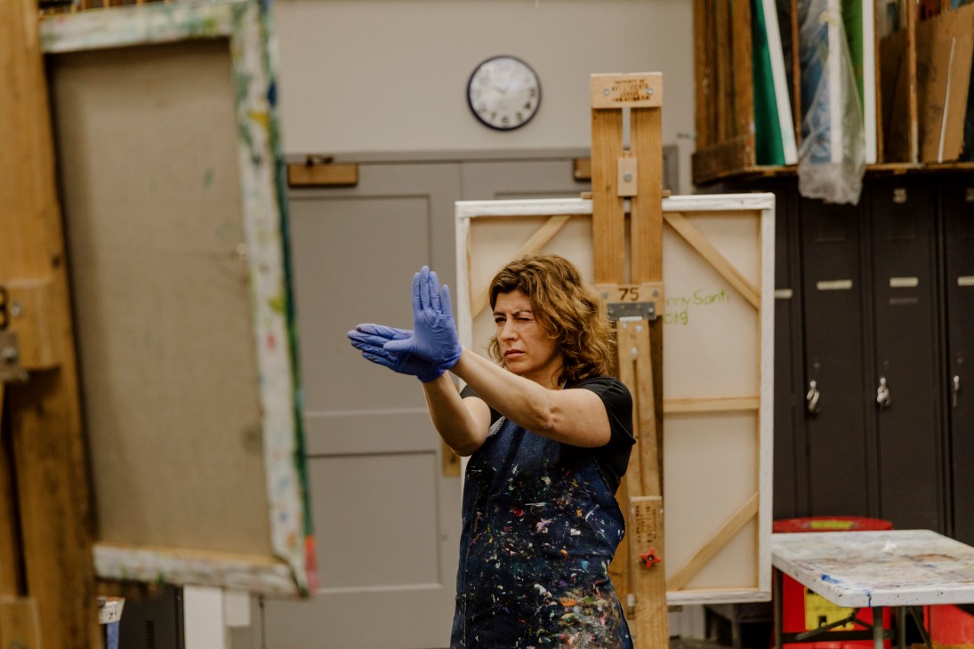 Student in James Little's non-objective painting class wearing blue gloves, gesturing toward a canvas in a studio.