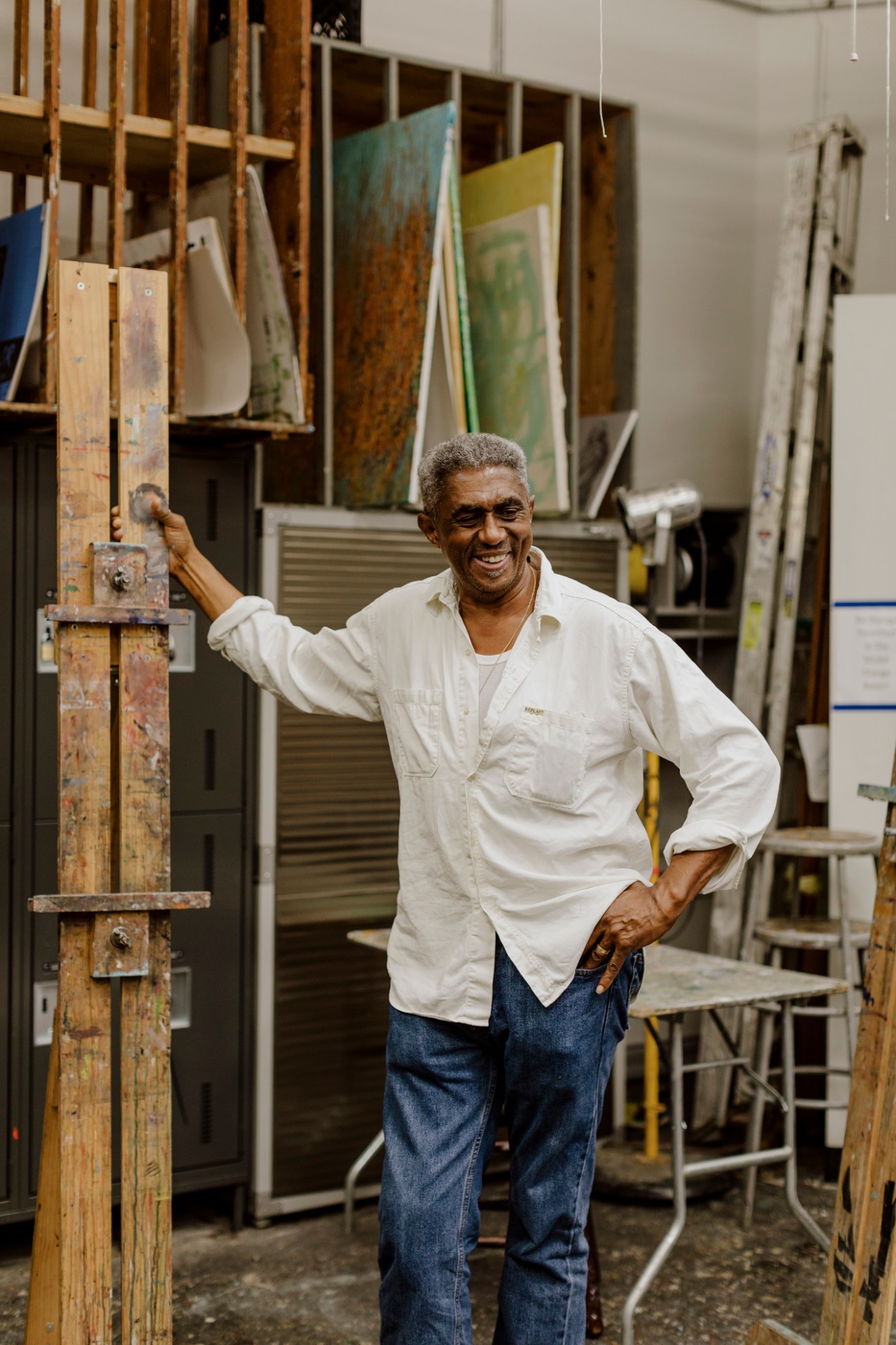 Instructor James Little smiles in his studio surrounded by wooden storage racks and paintings.