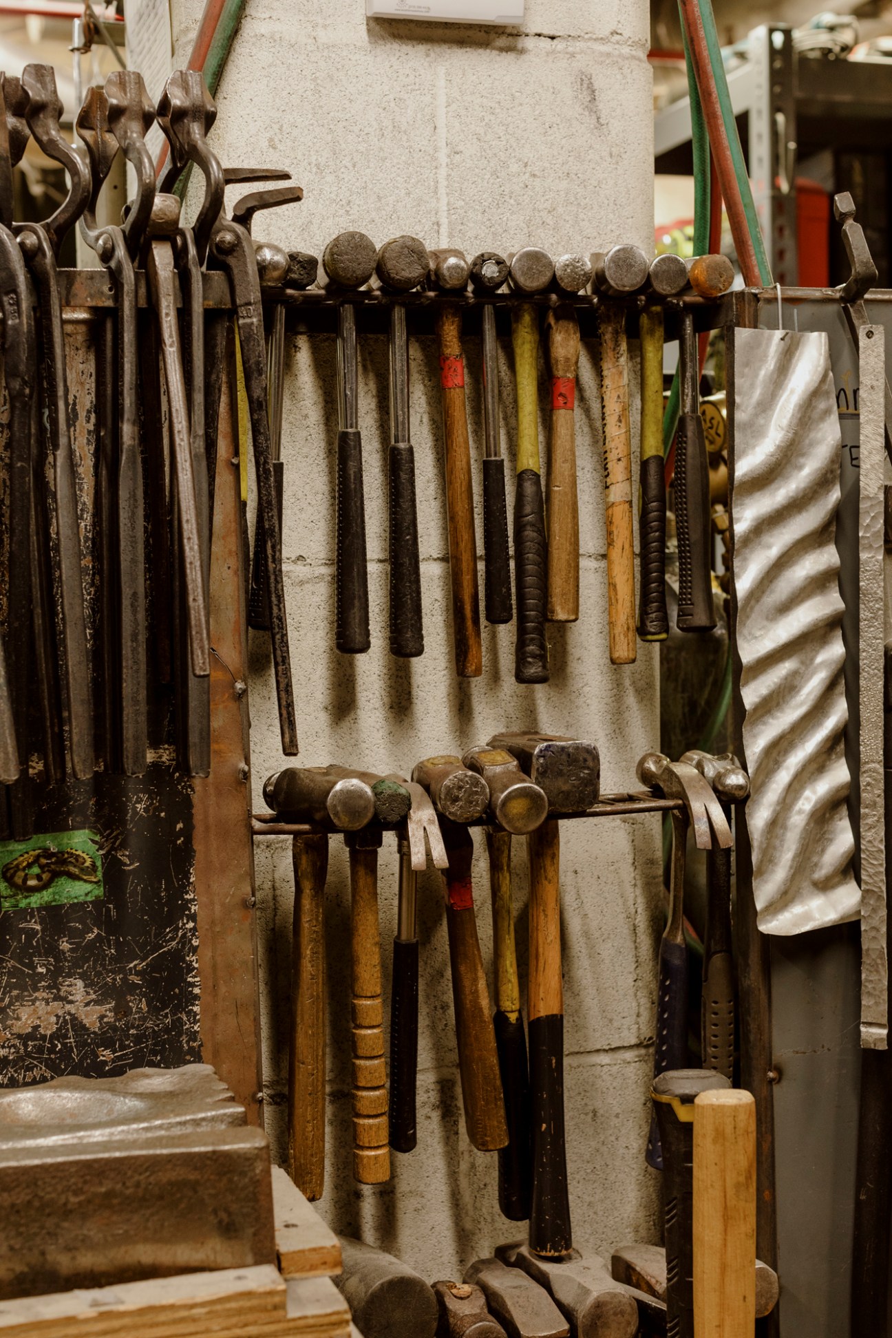 Organized metalwork tools hanging on a studio wall, including hammers, chisels, and punches with wooden handles.