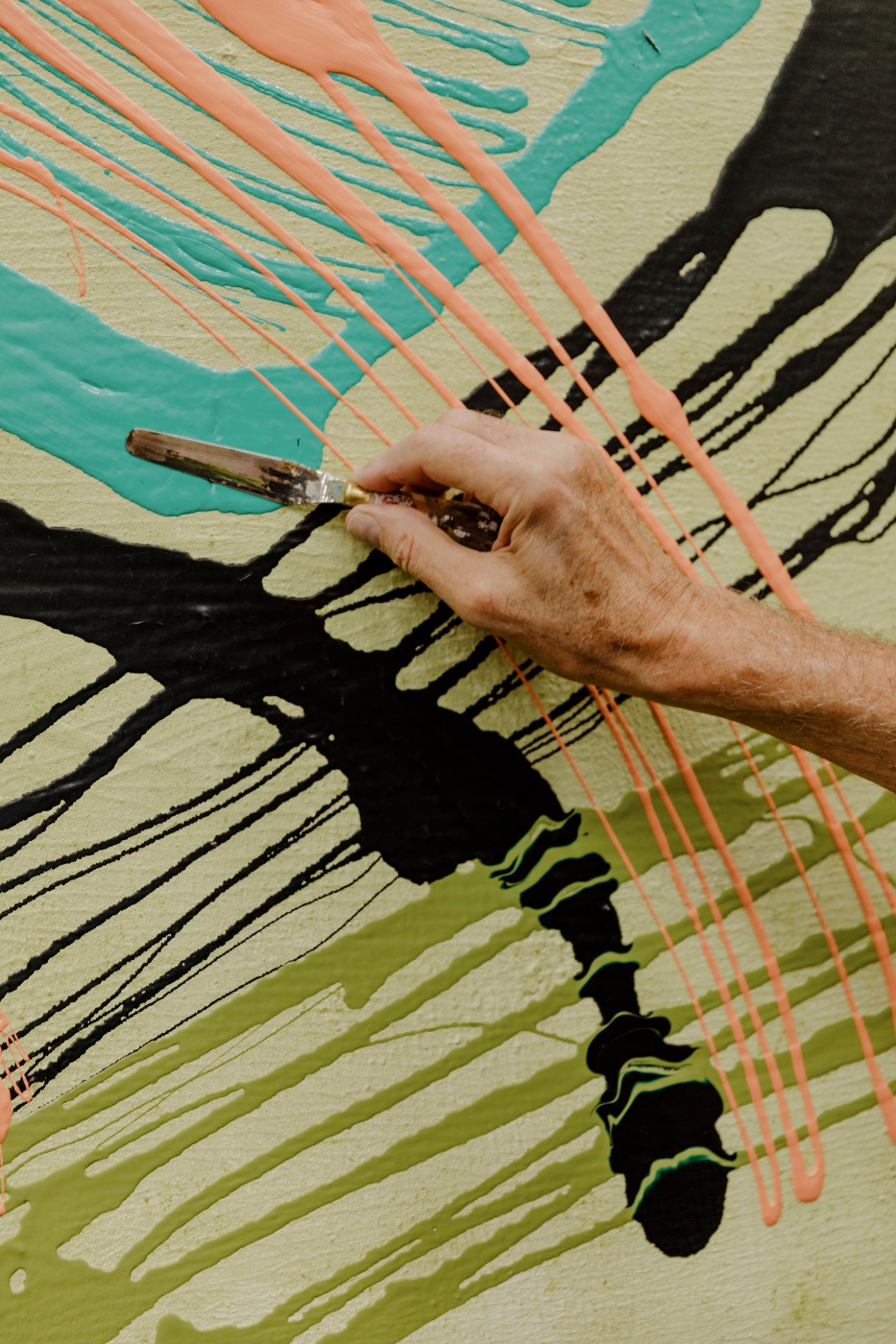 Artist's hand holding a brush painting colorful abstract lines on canvas.
