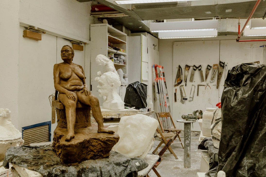 Artist's plaster studio with bronze and white sculptural busts, tools, shelving, and work surfaces.