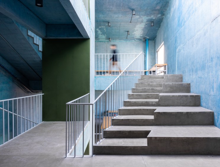 Interior stairway of Pilares community center with concrete steps, white railings, and blue painted walls