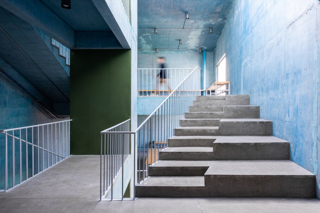 Interior stairway of Pilares community center with concrete steps, white railings, and blue painted walls