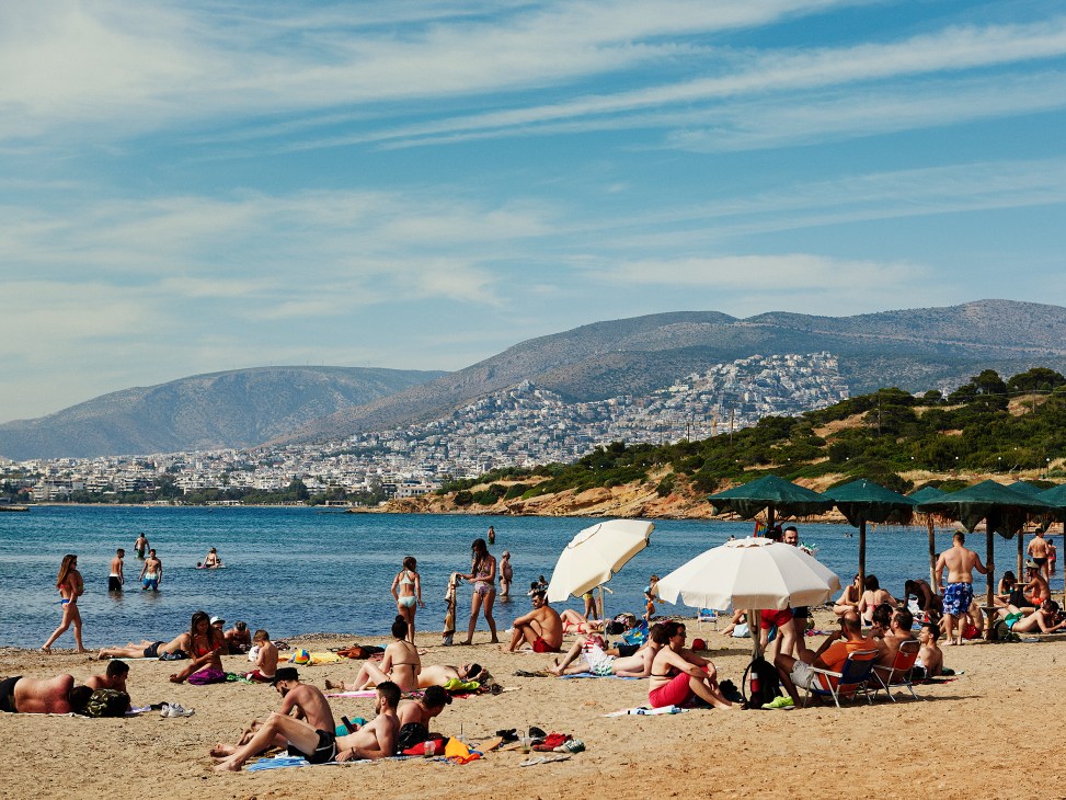 Beachgoers sunbathing and swimming at a sandy beach with umbrellas and mountains in the background