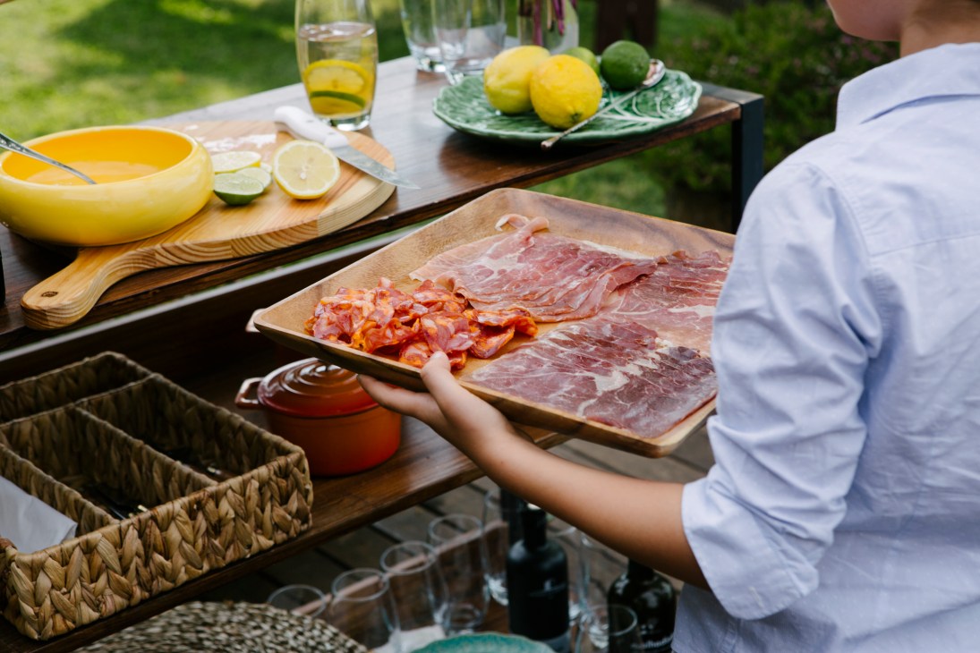 Person arranging Portuguese presunto ham and chouriço sausage on wooden cutting board