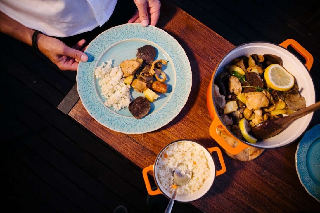 Hands serving rojões à moda do Minho stew with rice and vegetables on blue patterned plate