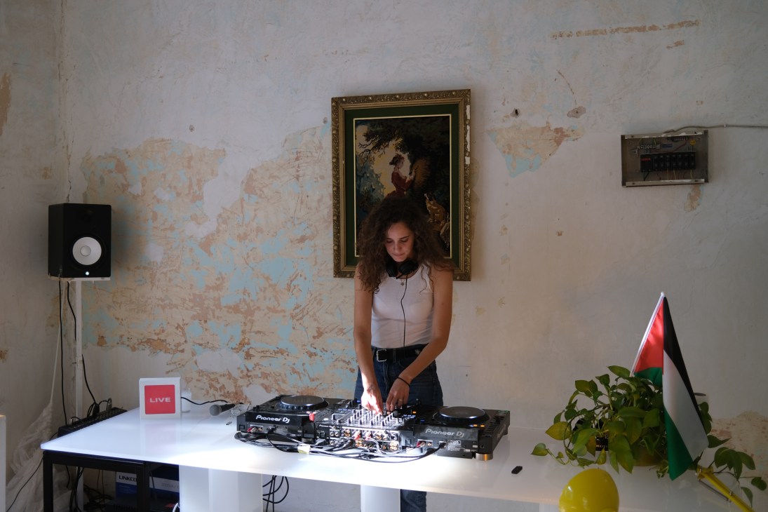 DJ performing at Radio AlHara with turntables and mixing equipment in studio with weathered walls
