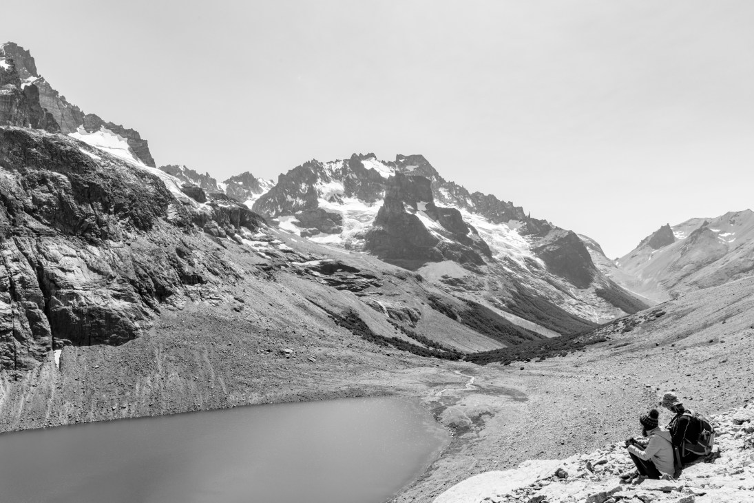 Two hikers sitting by a glacial lake surrounded by snow-capped mountains in Patagonia