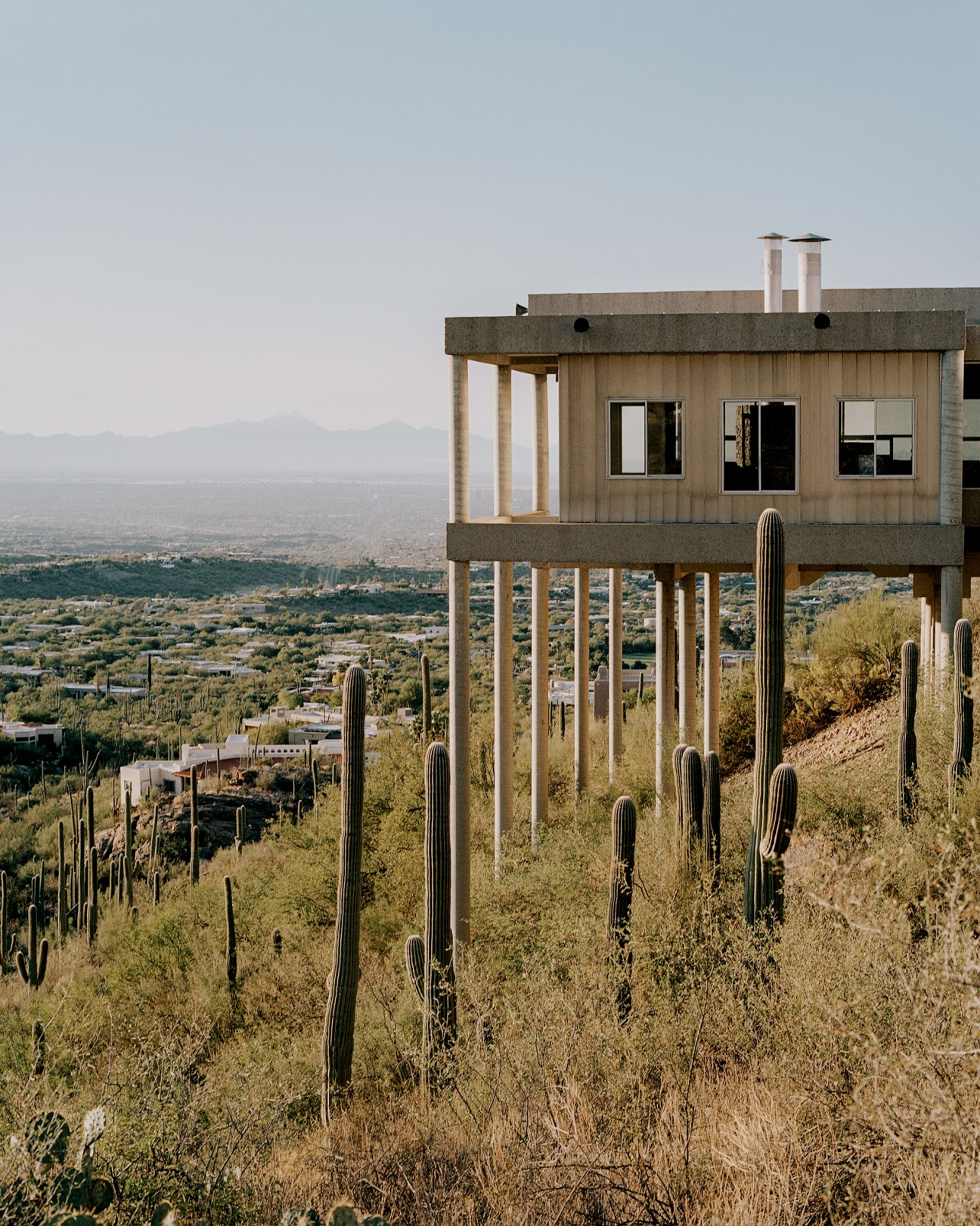 Thin concrete columns supporting modernist house structure above rocky desert ground
