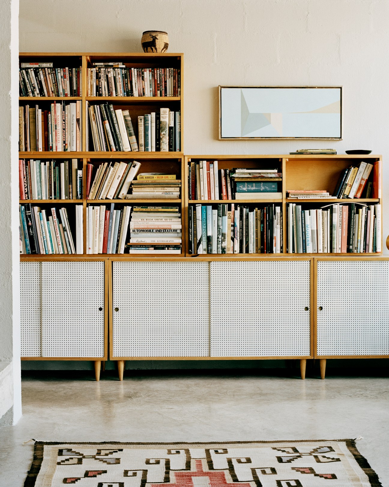 Modern living room with built-in wooden bookshelves, concrete surfaces and framed artwork on white wall